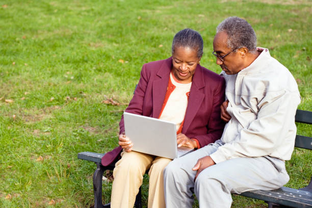 Senior African couple using laptop on bench outdoors